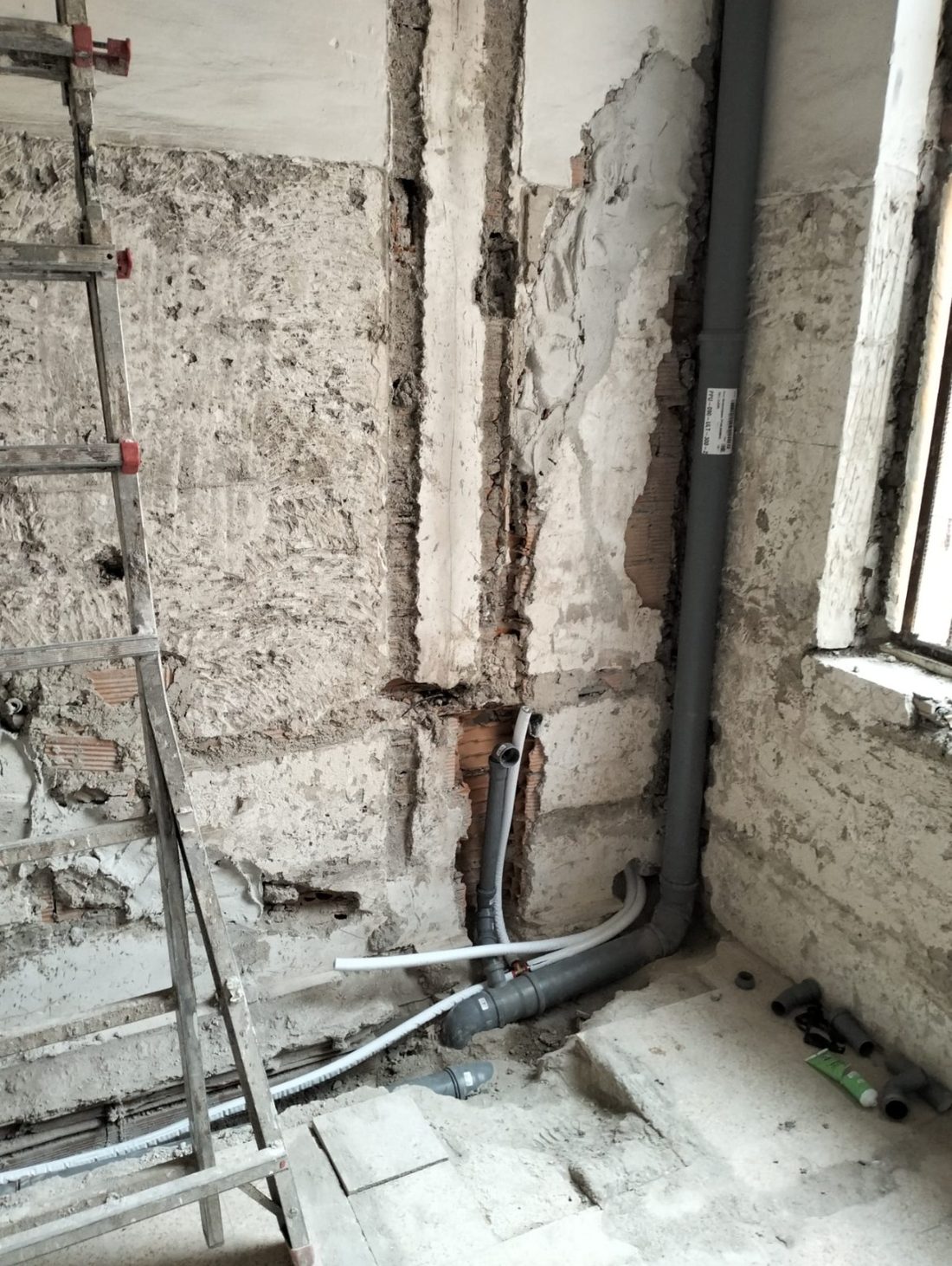 Tracce aperte nel muro di un bagno in ristrutturazione, con la nuova tubazione di scarico Geberit a innesto
