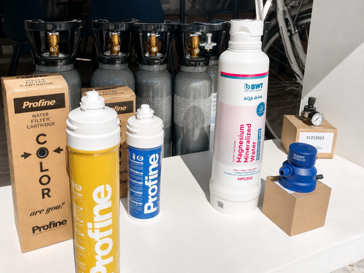 Cartucce Profine e filtro BWT AQA drink al banco del negozio, con le bombole CO₂ sullo sfondo